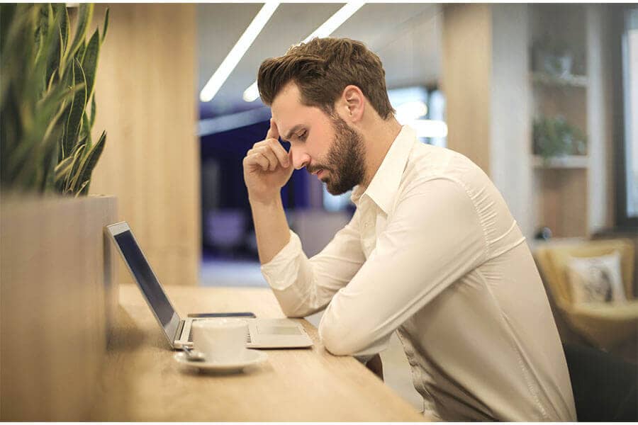Mann vor Computer sitzend hält sich wegen Kopfschmerzen Hand an den Kopf